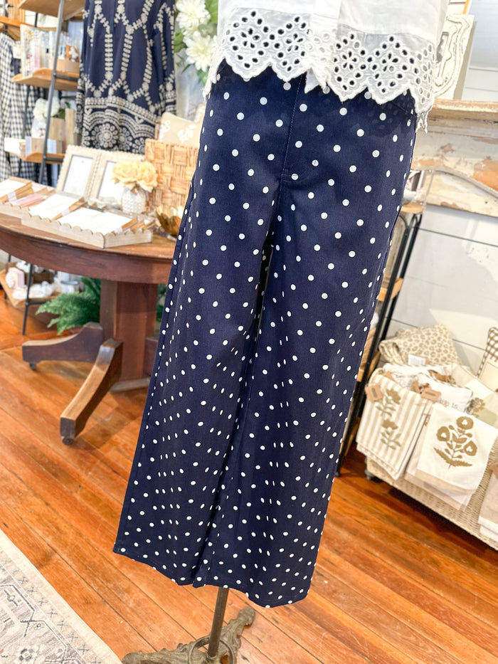 Navy blue pants with white polka dots on a mannequin in a store setting.
