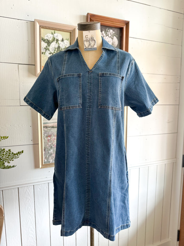 Blue denim dress on a mannequin against a white paneled wall.