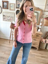Woman taking a mirror selfie wearing a pink shirt and blue jeans in a home setting.