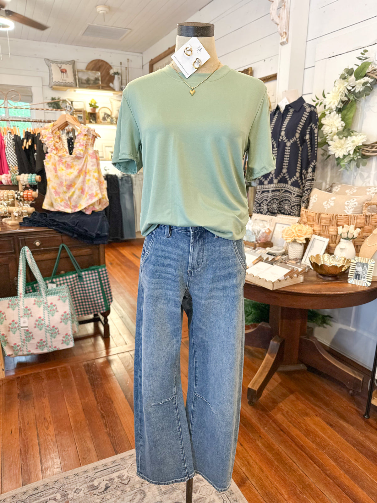 Mannequin wearing a green shirt and blue jeans in a store setting with various items in the background.