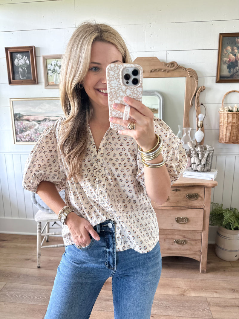 Woman taking a mirror selfie wearing a patterned blouse and blue jeans in a home setting.
