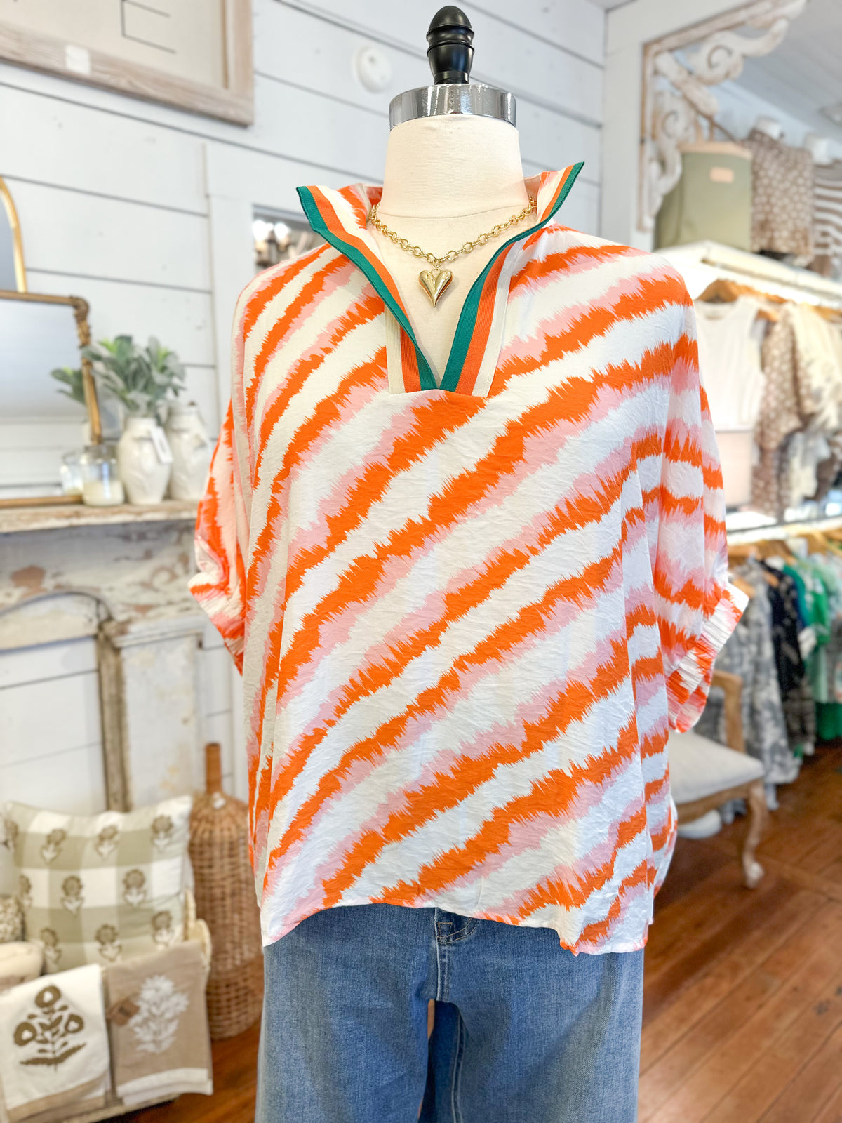 Mannequin wearing an orange and white striped top with a green trim in a store setting.