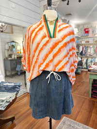 Mannequin wearing an orange and white striped poncho with a denim skirt in a store setting.