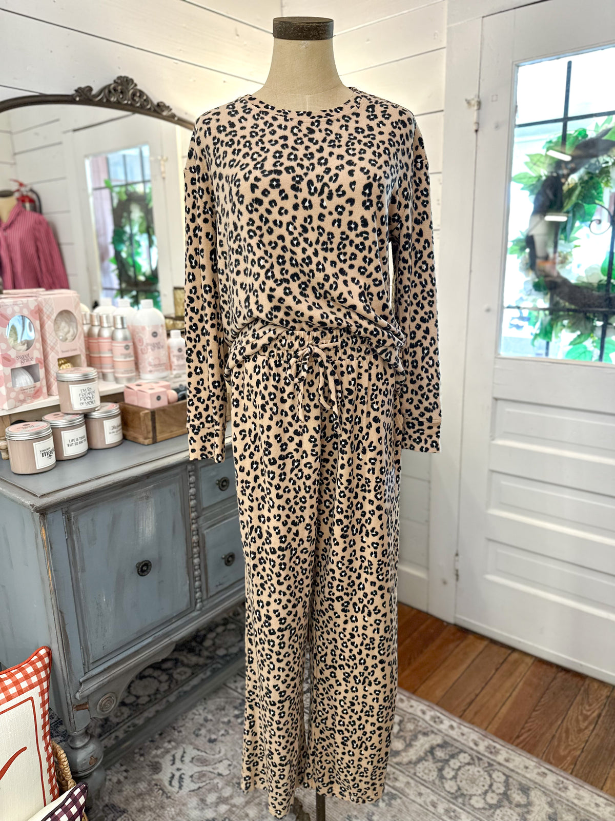 A beige and black leopard print two-piece set consisting of a long-sleeve top and matching wide-leg pants, displayed on a mannequin in a boutique setting.