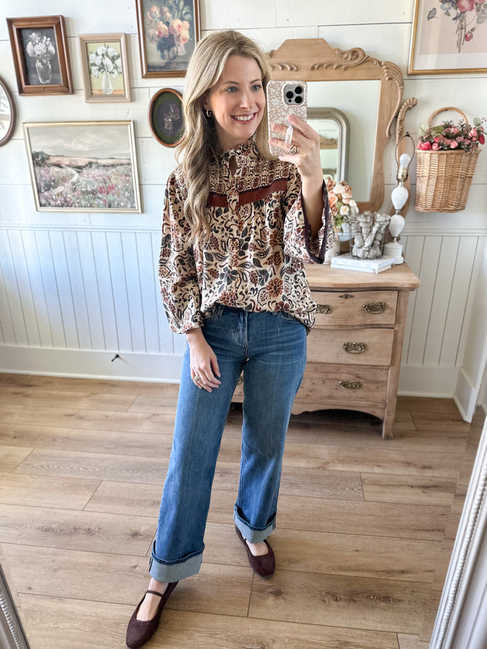 Woman taking a mirror selfie wearing a patterned blouse and jeans in a home setting.