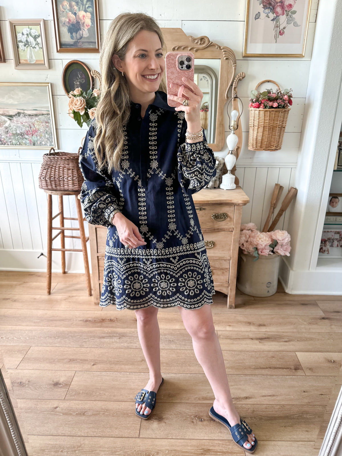 Woman taking a mirror selfie wearing a navy dress with white patterns in a home setting.