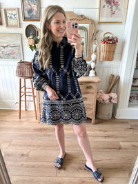 Woman taking a mirror selfie wearing a navy dress with white patterns in a home setting.