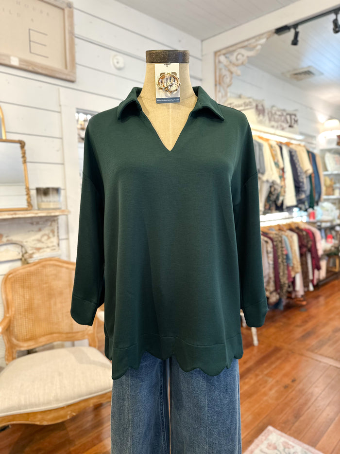 Green long-sleeve top on a mannequin in a store setting scallop hem on top 