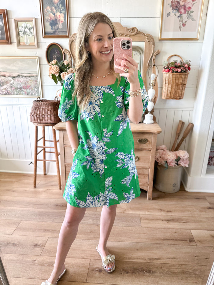 Woman taking a mirror selfie wearing a green floral dress in a home setting.