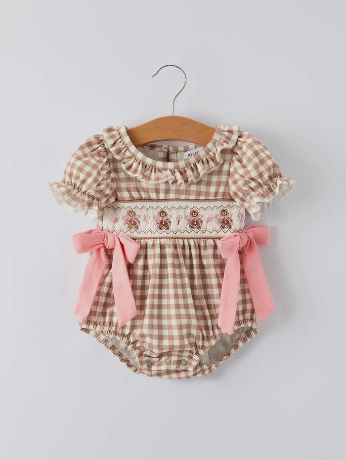 Baby romper with plaid pattern and pink bows on a hanger against a light gray background