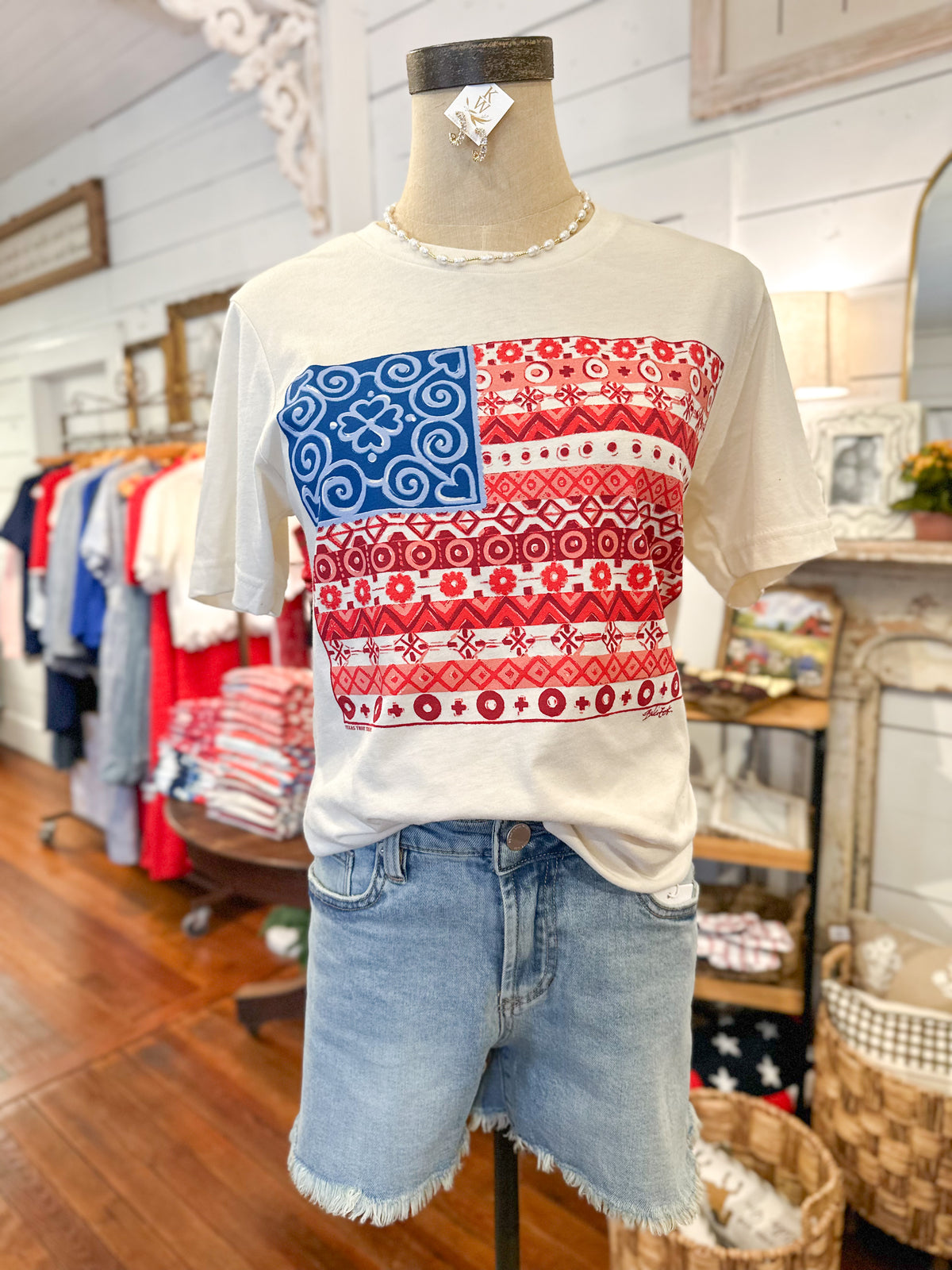 Mannequin wearing a white t-shirt with a red, white, and blue pattern in a store setting.