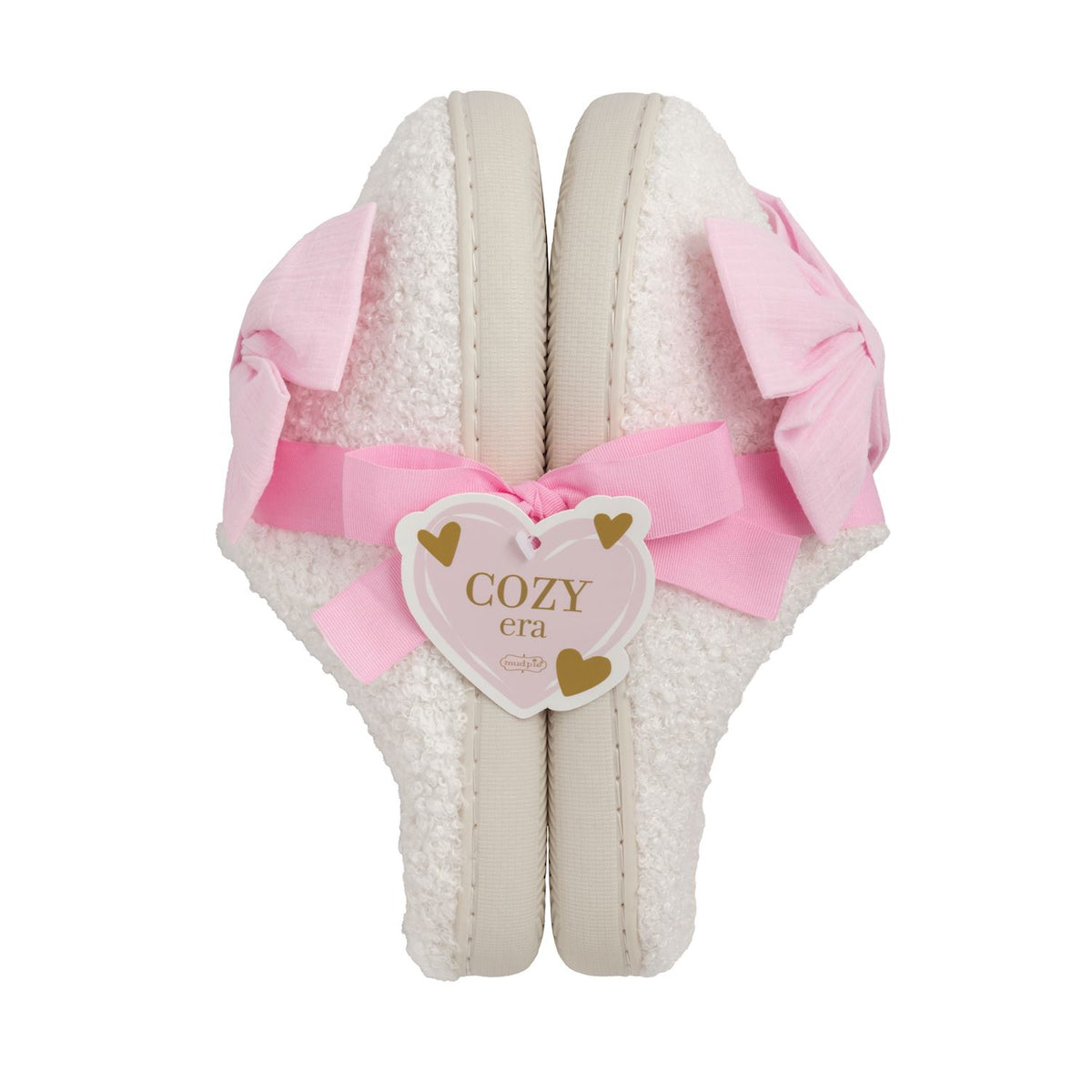 White slippers with pink bow and 'COZY era' label on a white background mud pie 