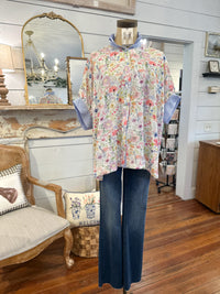 Mannequin wearing a floral blouse and jeans in a store setting with furniture and decor.