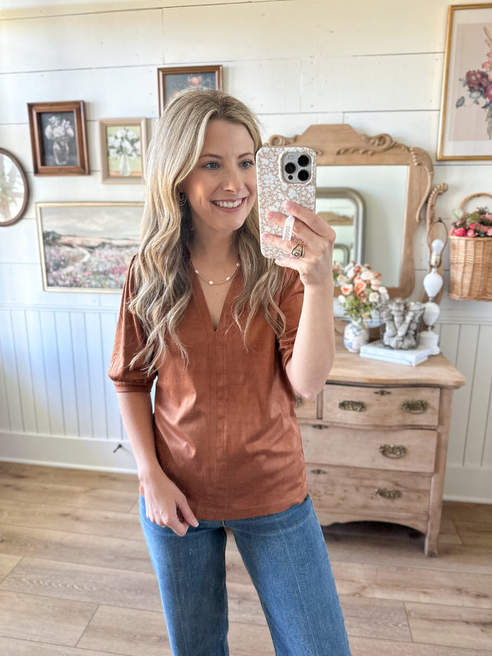 Woman taking a mirror selfie wearing a brown top and blue jeans in a home setting.