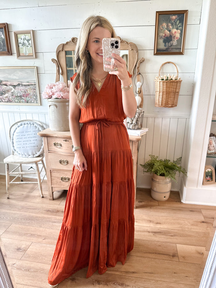 Woman in a rust-colored dress taking a mirror selfie in a home setting.