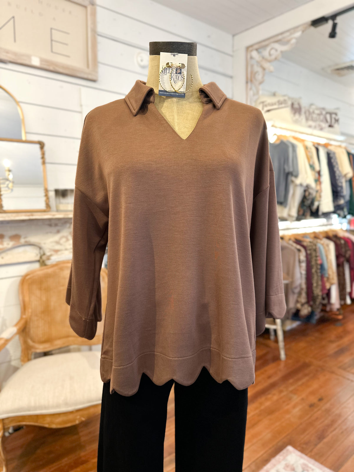 Brown sweater on a mannequin in a store setting with clothing racks in the background