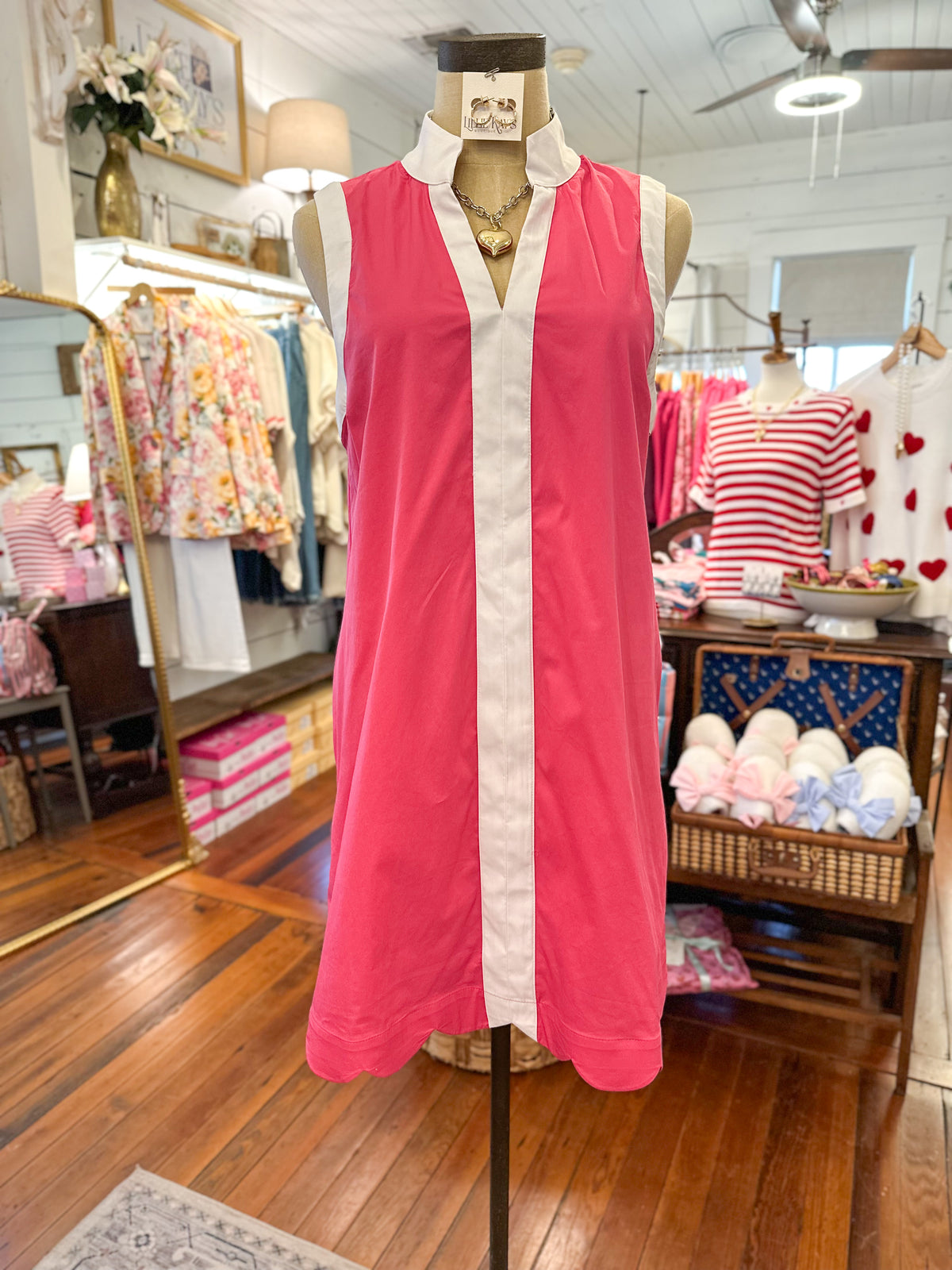 Pink dress on a mannequin in a store setting with various clothing items in the background.