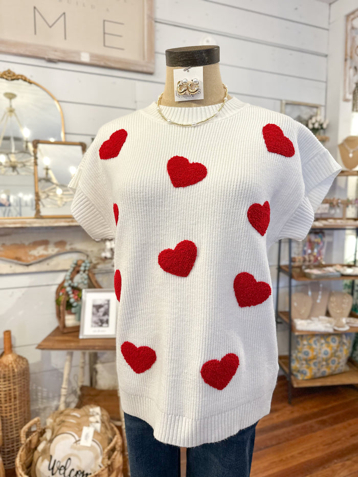 White sweater with red heart patterns on a mannequin in a store setting.