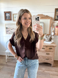 Woman taking a mirror selfie in a room with wooden floors and furniture. Brown silky soft button down top with rolled sleeves 