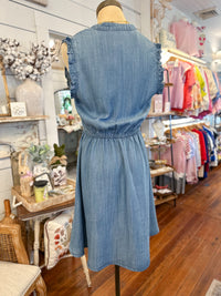Blue denim dress on a mannequin in a store setting with colorful clothing in the background.