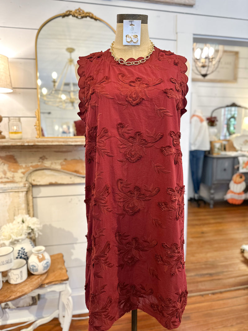 burgundy floral applique design dress on a mannequin in a store setting with mirrors and decor.