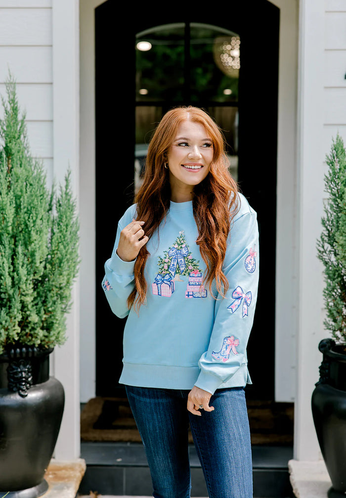 Woman wearing a light blue sweatshirt with colorful designs standing in front of a house entrance.