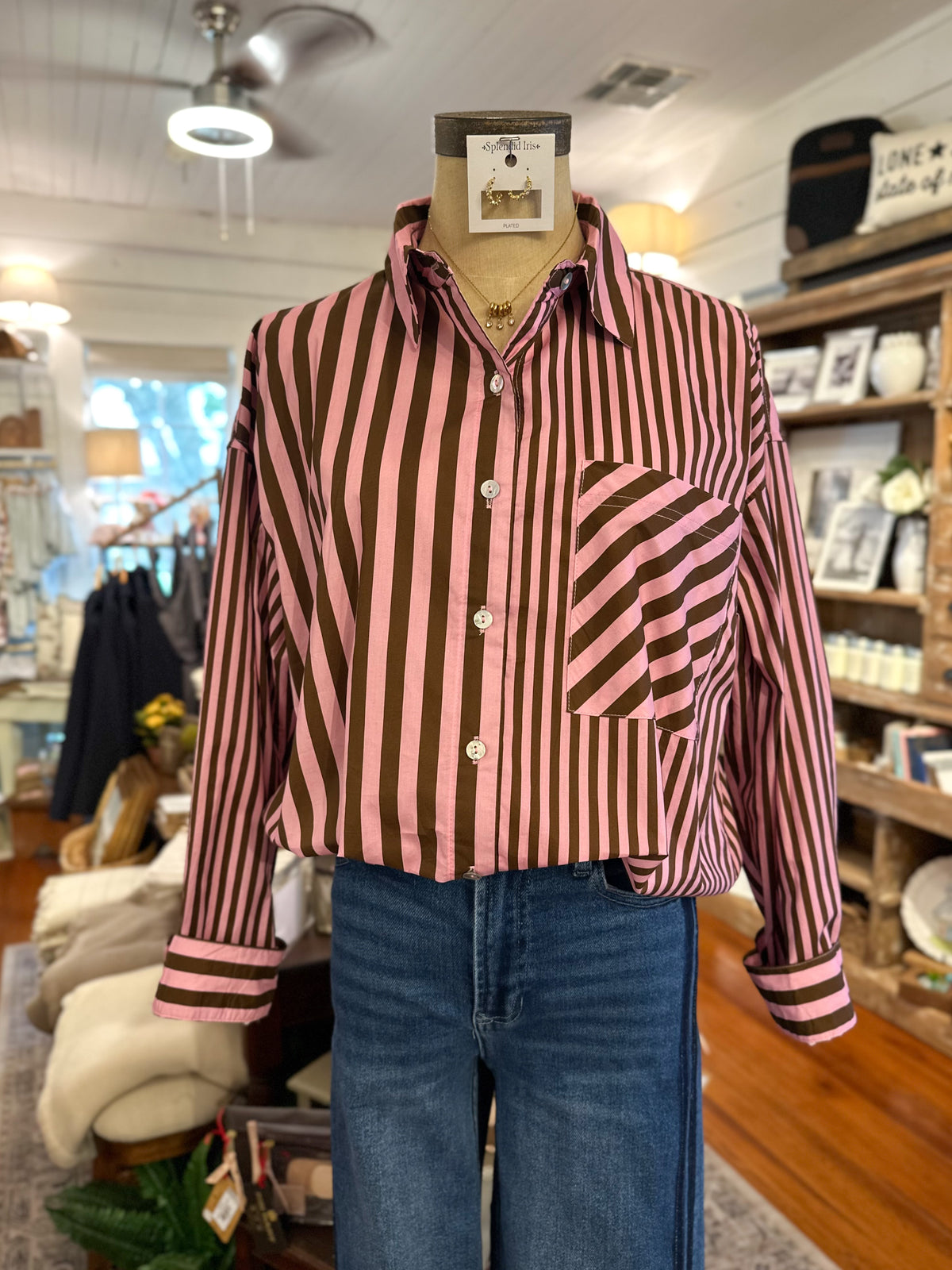 A pink and brown vertically striped button-up shirt with diagonal striped pocket detail, displayed on a mannequin torso with blue jeans in a retail store setting.