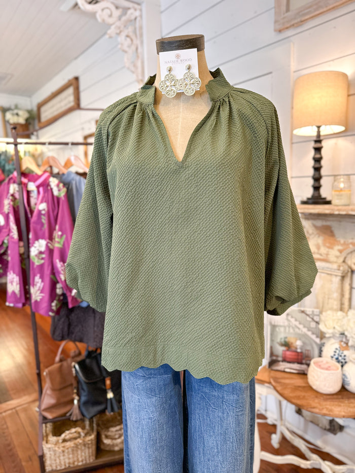 Green blouse on a mannequin with blue jeans in a store setting umgee green top with scallop hem 