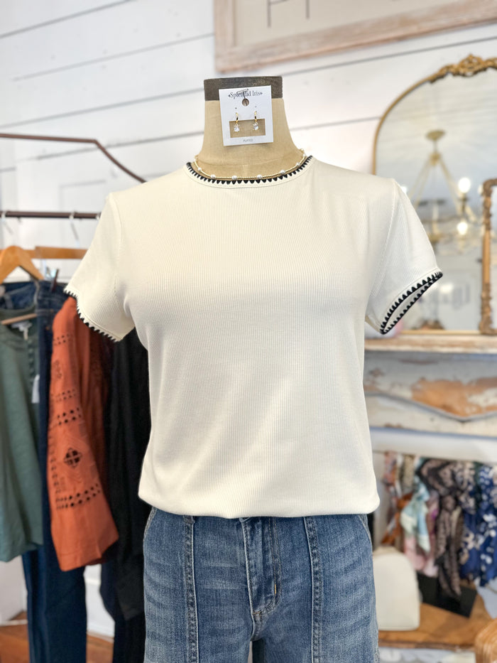 Mannequin wearing a white t-shirt with black trim in a clothing store setting.
