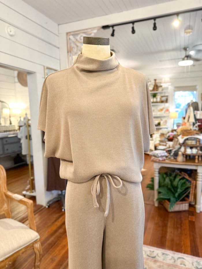 Mannequin wearing a beige turtleneck top and pants in a store setting.