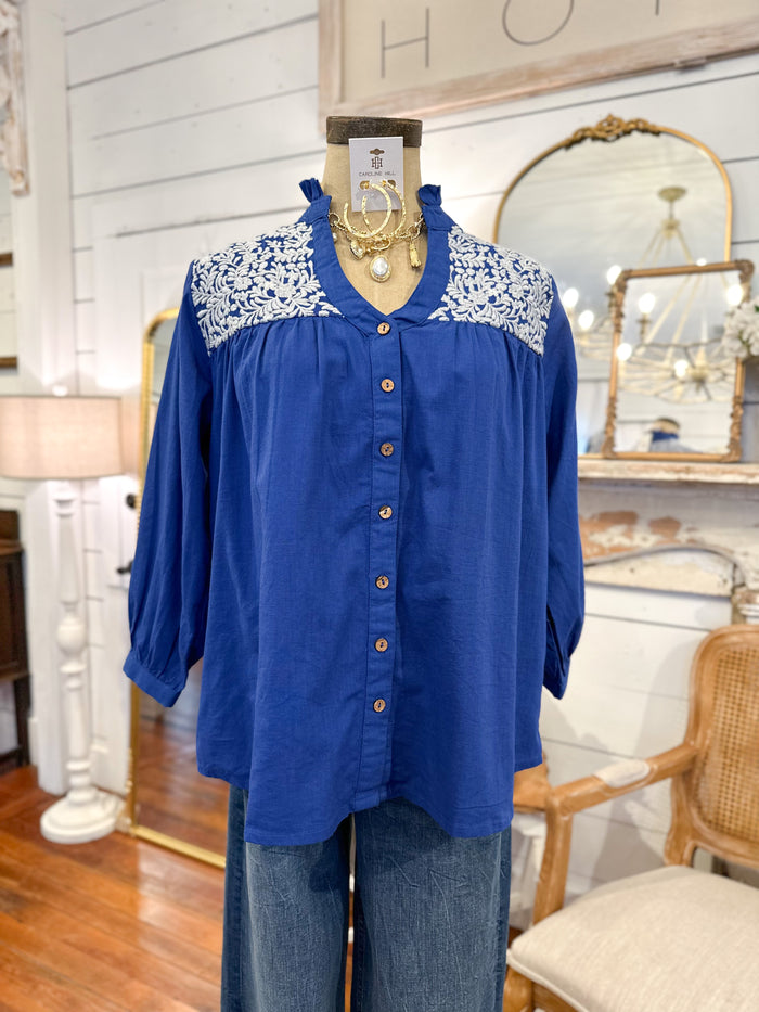 Blue blouse with lace collar on a mannequin in a room with mirrors and a lamp.