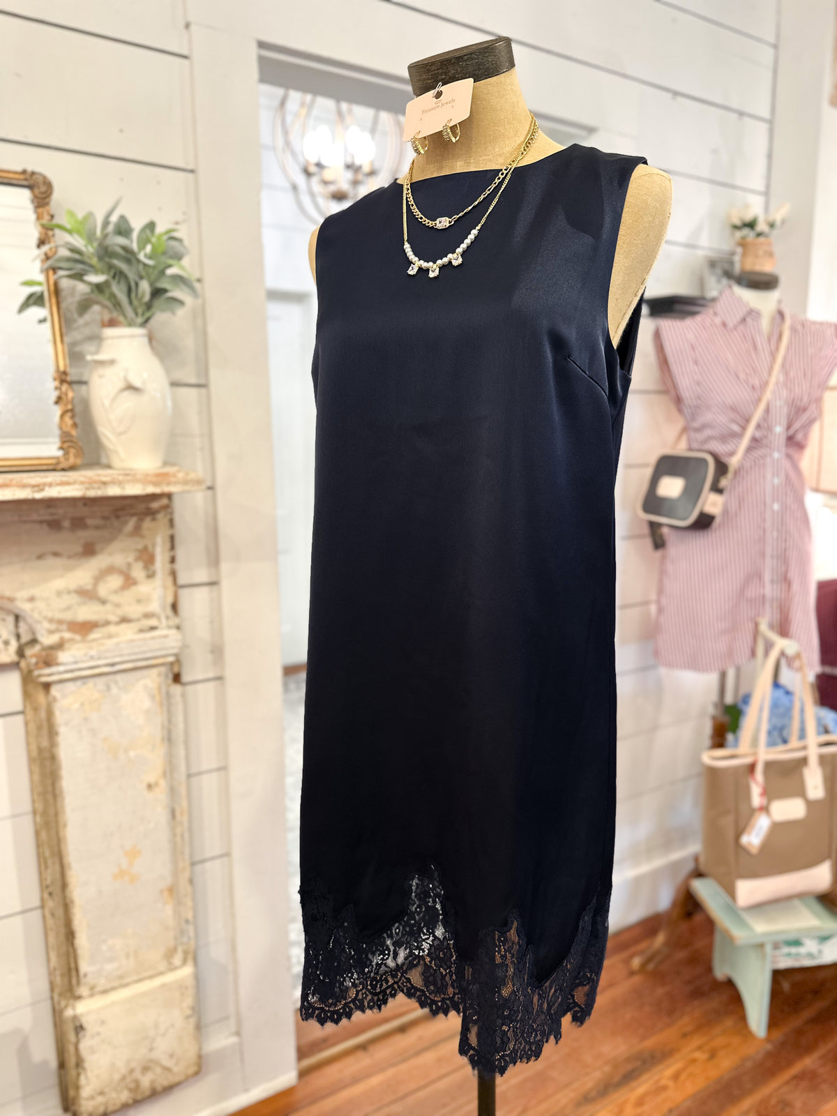 A sleeveless navy satin dress with a navy lace hem, displayed on a mannequin in a boutique setting.