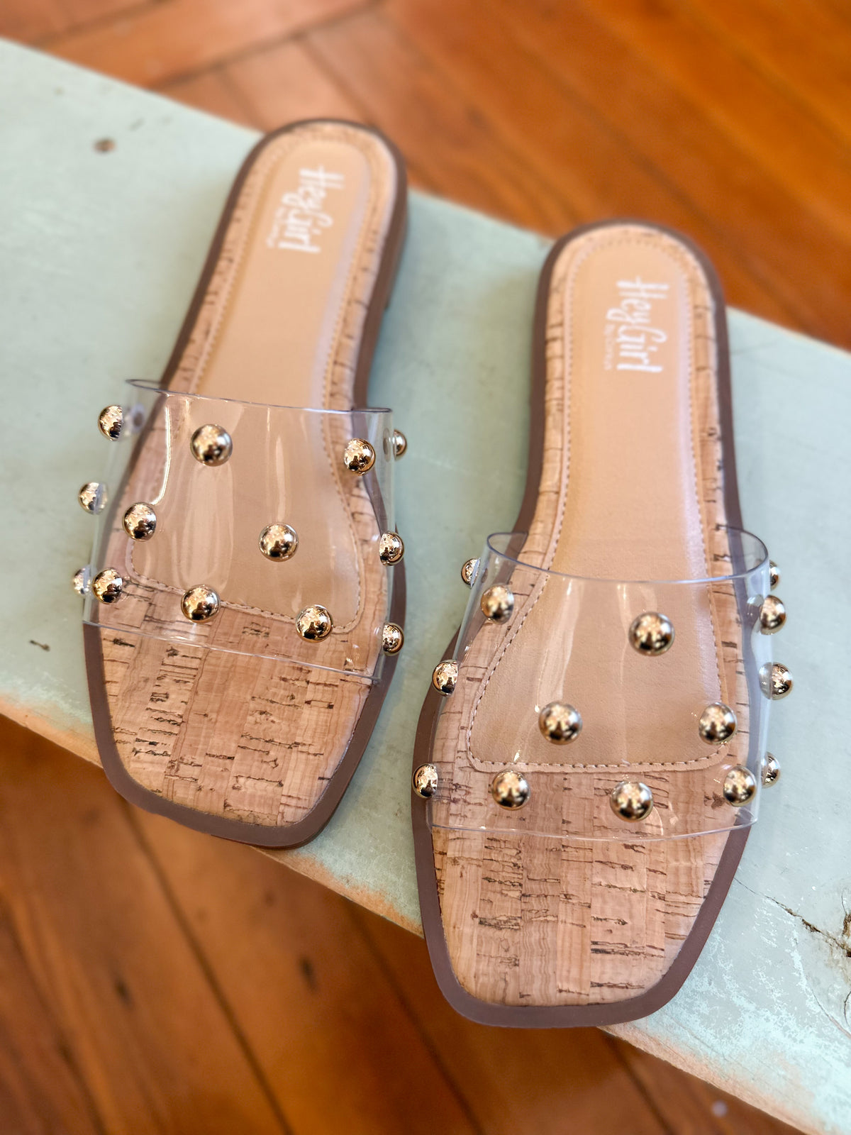 Clear slide sandals with gold studs on a light green surface.