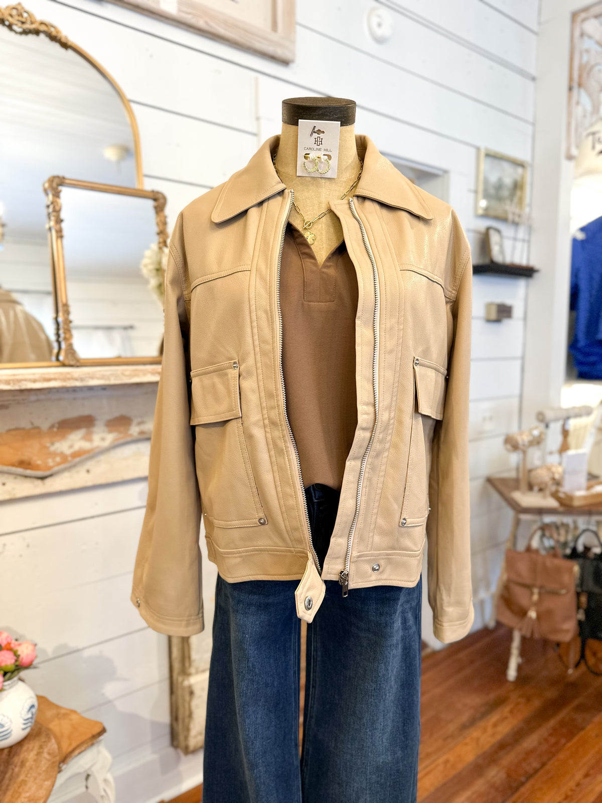 Tan faux leather jacket on a mannequin in store setting 
zips up and has button snap on the bottom