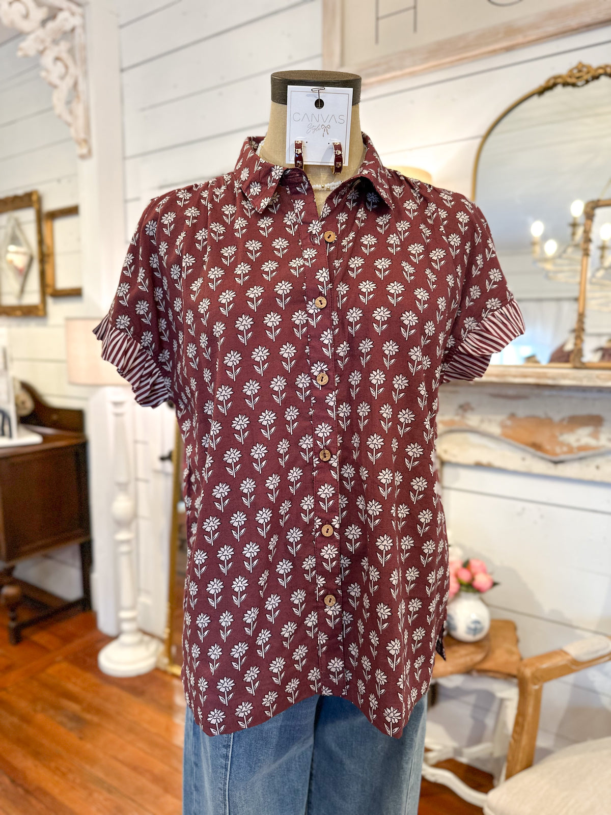 Maroon shirt with white floral pattern on a mannequin against a decorative interior background maroon button down block print top