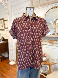 Maroon shirt with white floral pattern on a mannequin against a decorative interior background maroon button down block print top