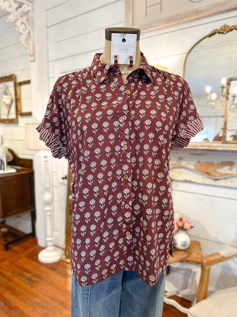 Maroon shirt with white floral pattern on a mannequin against a decorative interior background maroon button down block print top