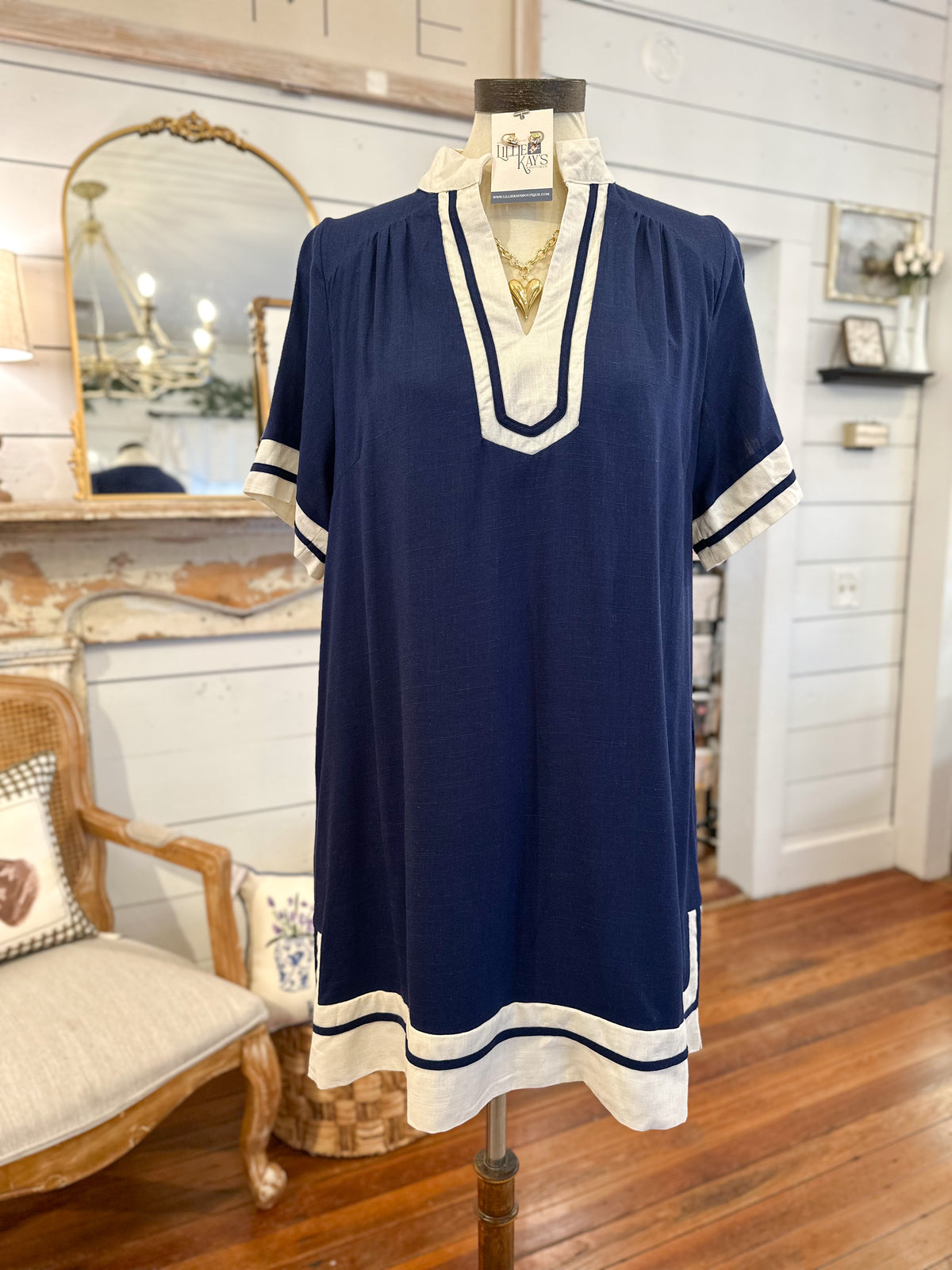 Navy blue dress with white trim on a mannequin in a room with wooden floor and chair.