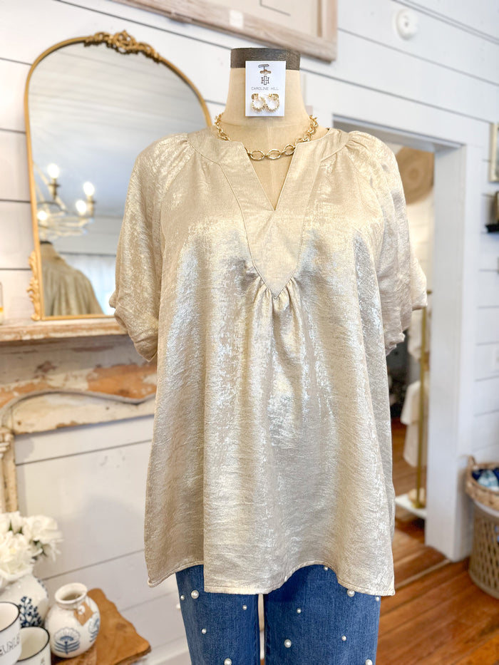 Mannequin wearing a light-colored blouse with a gold necklace in a store setting.