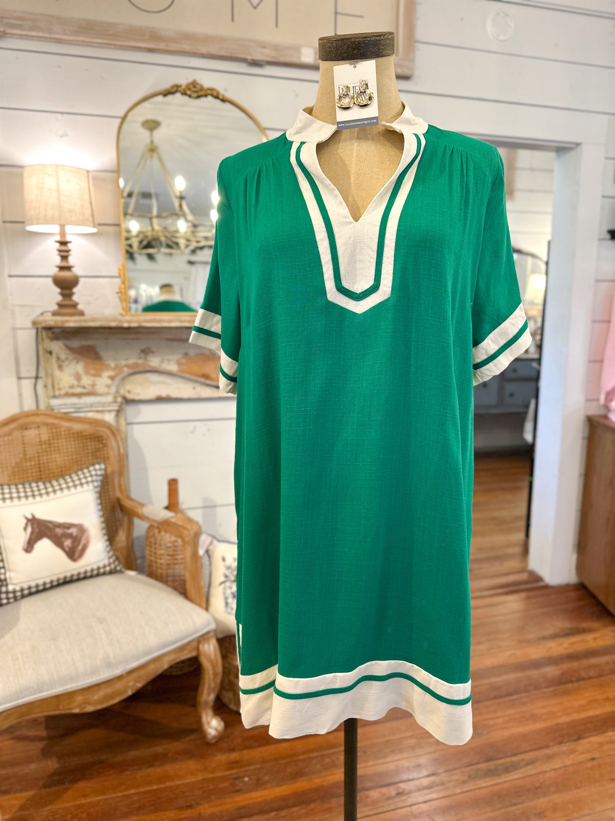 Green dress with white trim on a mannequin in a room with wooden floor and furniture.