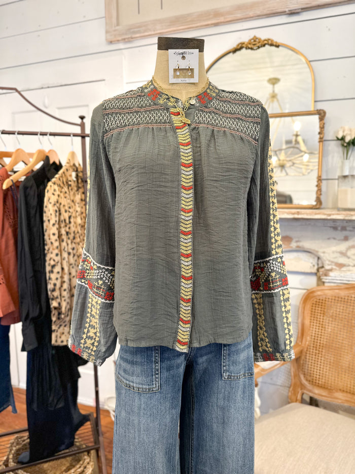 Green blouse with colorful patterns on a mannequin in a clothing store.