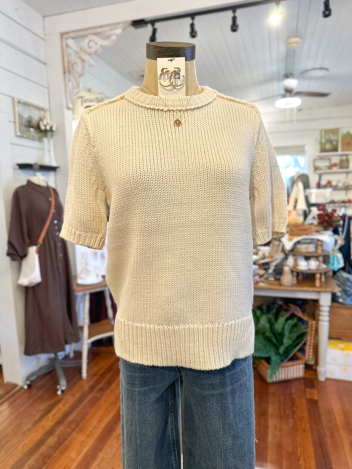 Beige knitted vest on a mannequin in a store setting