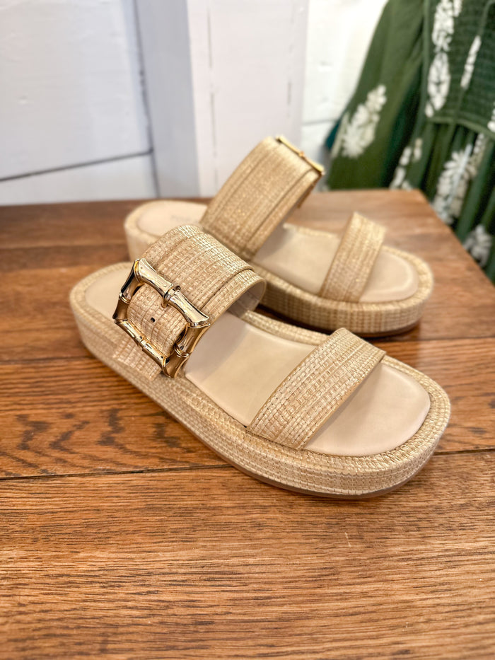 Beige sandals with gold buckle on a wooden surface