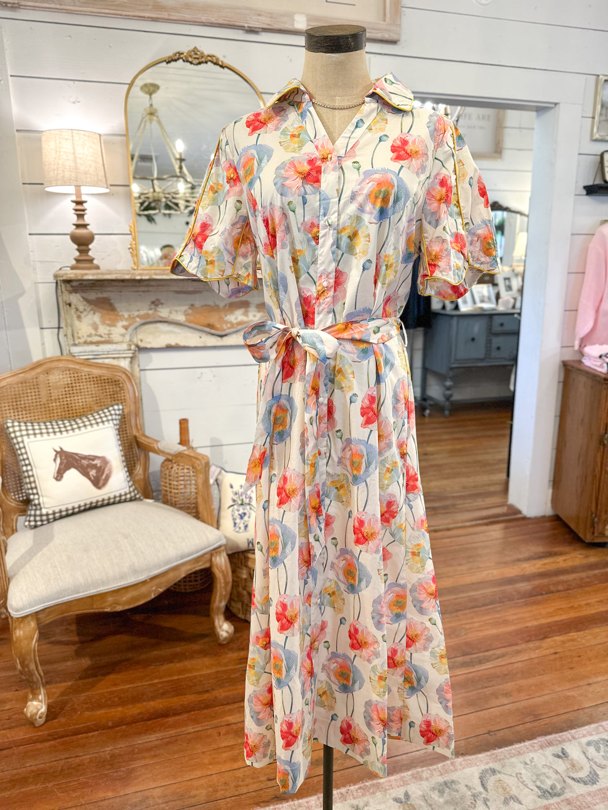 Floral dress on a mannequin in a room with wooden floor and chair.