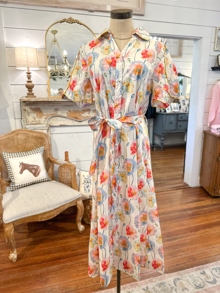 Floral dress on a mannequin in a room with wooden floor and chair.