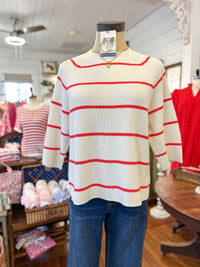Mannequin wearing a white sweater with coral red stripes in a store setting