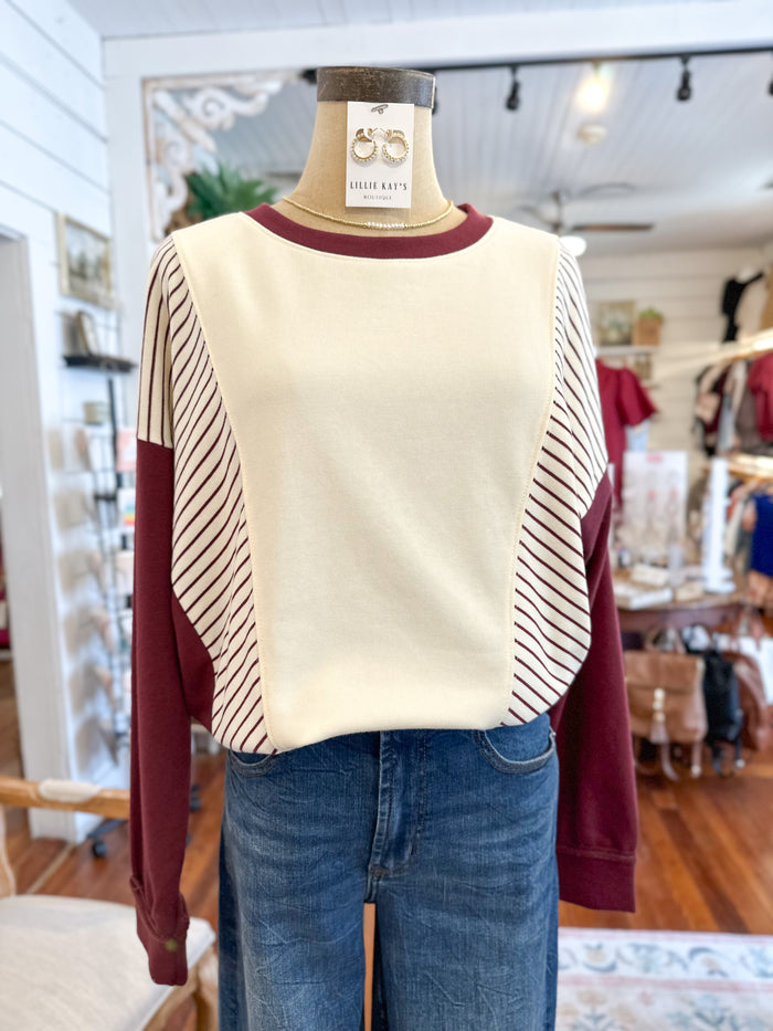 Mannequin wearing a cream sweater with burgundy sleeves and blue jeans in a store setting.