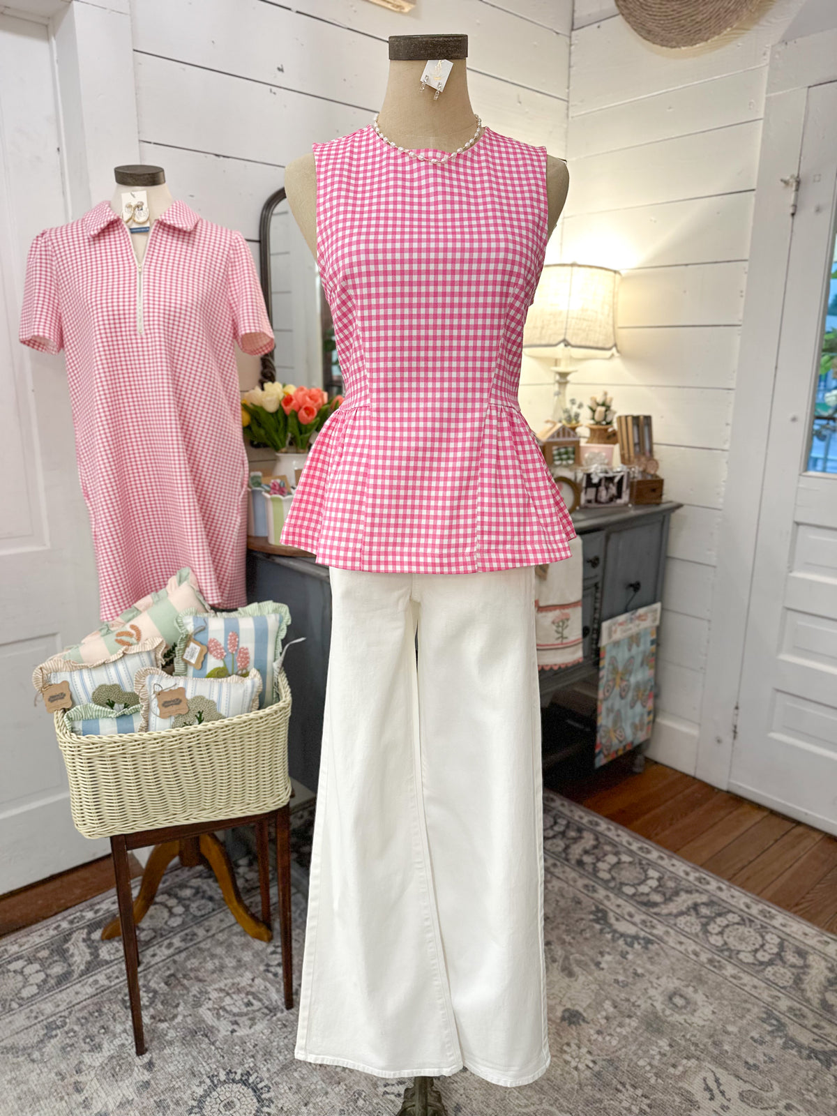 Mannequin wearing a pink checkered top and white pants in a room with decor elements.