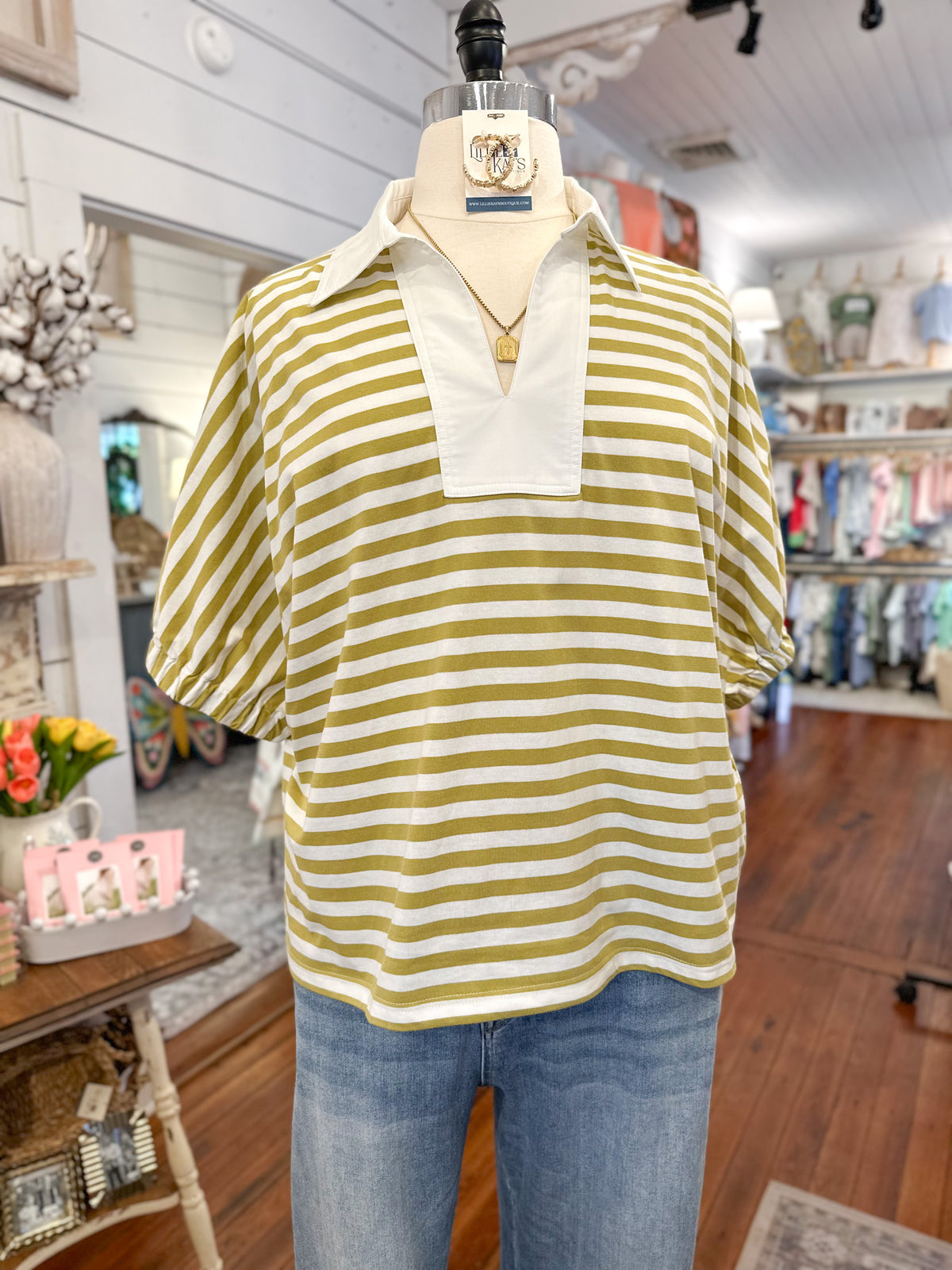 Mannequin wearing a yellow/green and white striped shirt with a collar in a store setting.
