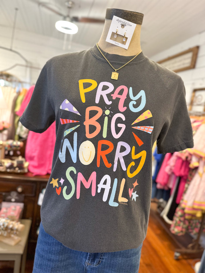 light grey  t-shirt with colorful text 'PRAY BIG WORRY SMALL' on a mannequin in a store setting.